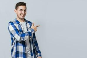 sonriente hermoso hombre recomendando alguna cosa con su dedos. caucásico hermoso chico señalando su dedo a un blanco espacio, sonriente adolescente señalando dedos a el lado foto