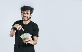 Handsome man pointing at the money in his hand isolated, a person pointing at money bills in his hand, concept of earnings and savings photo
