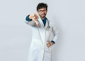 Doctor gesturing disapproval isolated. Unhappy doctor with thumb down isolated. Male doctor disapproving with fingers photo