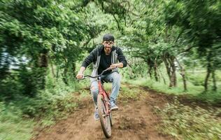 retrato de un chico en gorra montando un bicicleta en un país camino, persona montando un bicicleta en el campo, ciclista persona en su bicicleta en un país la carretera bosque. Adolescente chico montando un bicicleta en el campo foto