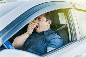 A sleepy driver at the wheel, a tired person while driving, Tired driver yawning, concept of man yawning while driving photo