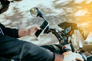 manos de motocicleta hombre mensajes de texto en el teléfono. de cerca de motociclista mensajes de texto en el teléfono. concepto de motociclista utilizando célula teléfono mientras conducción foto
