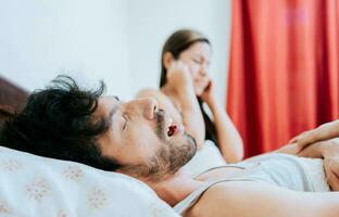 Snoring man in bedroom and wife covering her ears. Husband snoring while the wife suffers and covers her ears. Sleep apnea concept photo