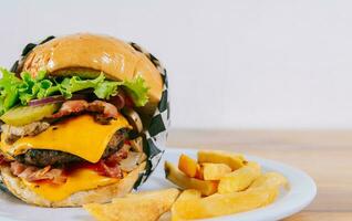 hecho en casa hamburguesa con francés papas fritas en un plato en de madera mesa. grande hamburguesa con queso con papas fritas servido con Copiar espacio foto