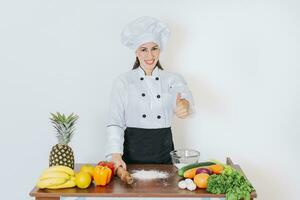 Chef woman holding bread rolling pin with thumb up, Smiling chef woman holding rolling pin on vegetable table, Concept of chef woman holding bread rolling pin photo