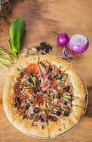 Top view of supreme pizza with olives and vegetables on wooden table. Delicious supreme pizza with vegetables on wooden background photo