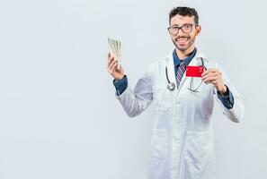 contento joven médico participación crédito tarjeta y dinero aislado. hermoso médico participación dinero y crédito tarjetas aislado foto