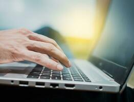 Close-up of a man's hands working on his laptop. Side view of hands working on laptop, Close up of a person's hands on the laptop keyboard outdoors, Close up of fingers on laptop keyboard photo