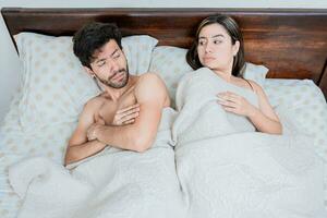 Upset couple in bed with crossed arms. Woman lying in bed upset with her husband. Angry man and woman in bed with crossed arms. Marriage problems concept photo