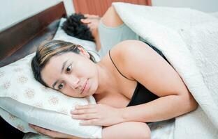 joven Pareja discutiendo y dormido aparte. concepto de Pareja problemas en cama. infeliz Pareja en cama dormido aparte, trastornado Pareja dormido en su espaldas foto