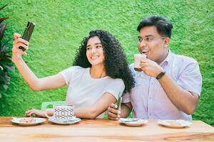 Pareja de amigos sentado disfrutando un café y tomando un autofoto dos contento amigos teniendo un café y tomando un selfie foto