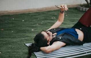 A girl lying on a bench with her cell phone, A woman lying on a bench with her cell phone, Girl lying down texting on her cell phone photo