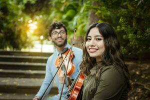 Two young violinists sitting outdoors looking at the camera. Portrait of two young violists sitting outside. Man and woman violinist sitting on the stairs. Concept of two young violinists photo