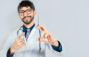 Handsome doctor holding and pointing a syringe isolated. Smiling doctor showing a syringe on isolated background. Doctor and vaccine concept photo