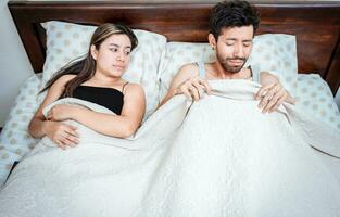 Worried husband with erectile dysfunction in bed. Disappointed man in bed with erectile dysfunction. Concept of couple sexual problems. Couple in bed upset about sexual dysfunction photo
