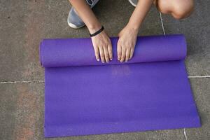 Woman hands rolling up the mat outside. Athlete woman's hands rolling up the mat after exercising. Concept of rolling up mat after exercise photo