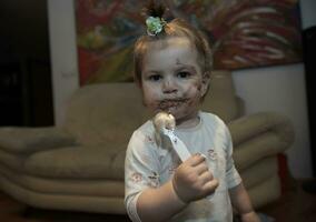 bebé niña comiendo su chocolate Desierto con un cuchara y haciendo un lío foto
