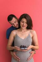 young pregnant couple holding newborn baby shoes photo