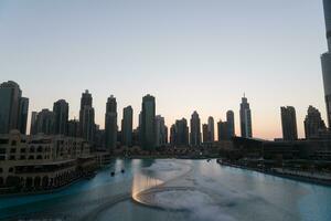 Dubai singing fountains at night lake view between skyscrapers. City skyline in dusk modern architecture in UAE capital downtown. photo