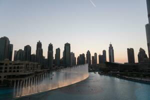 Dubai singing fountains at night lake view between skyscrapers. City skyline in dusk modern architecture in UAE capital downtown. photo