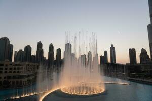 Dubai singing fountains at night lake view between skyscrapers. City skyline in dusk modern architecture in UAE capital downtown. photo