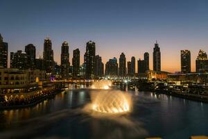 Dubai singing fountains at night lake view between skyscrapers. City skyline in dusk modern architecture in UAE capital downtown. photo