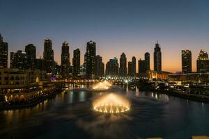 Dubai singing fountains at night lake view between skyscrapers. City skyline in dusk modern architecture in UAE capital downtown. photo