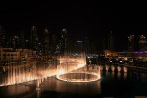 Dubai singing fountains at night lake view between skyscrapers. City skyline in dusk modern architecture in UAE capital downtown. photo