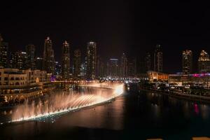 Dubai singing fountains at night lake view between skyscrapers. City skyline in dusk modern architecture in UAE capital downtown. photo