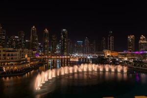 Dubai singing fountains at night lake view between skyscrapers. City skyline in dusk modern architecture in UAE capital downtown. photo