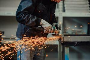 Heavy Industry Engineering Factory Interior with Industrial Worker Using Angle Grinder and Cutting a Metal Tube. Contractor in Safety Uniform and Hard Hat Manufacturing Metal Structures. photo