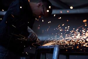 Heavy Industry Engineering Factory Interior with Industrial Worker Using Angle Grinder and Cutting a Metal Tube. Contractor in Safety Uniform and Hard Hat Manufacturing Metal Structures. photo