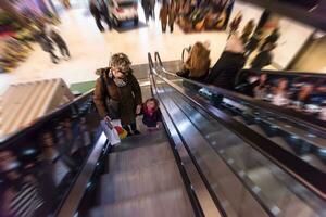 joven madre y su pequeño hija en escalera mecánica en compras centro comercial foto