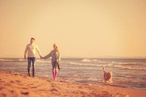 couple with dog having fun on beach on autmun day photo