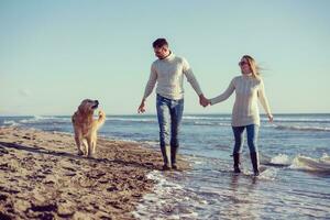 pareja con perro divirtiéndose en la playa el día del otoño foto