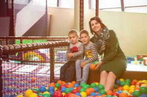 mamá joven jugando con niños en la piscina con bolas de colores foto