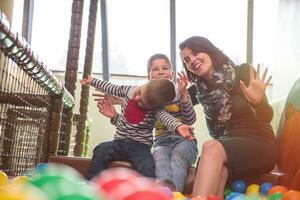 young mom playing with kids in pool with colorful balls photo