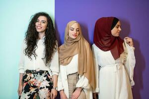 Group portrait of beautiful muslim women two of them in fashionable dress with hijab isolated on colorful background representing modern islam fashion and ramadan kareem concept photo