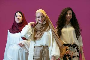 Group portrait of beautiful muslim women two of them in fashionable dress with hijab isolated on pink background representing modern islam fashion and ramadan kareem concept photo