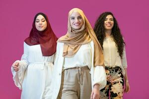 Group portrait of beautiful muslim women two of them in fashionable dress with hijab isolated on pink background representing modern islam fashion and ramadan kareem concept photo