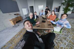 In a modern office, a group of businessmen gathers around a table during a meeting, capturing a moment of camaraderie and teamwork as they take a selfie photo