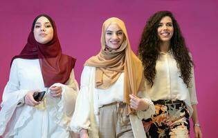 Group portrait of beautiful muslim women two of them in fashionable dress with hijab isolated on pink background representing modern islam fashion and ramadan kareem concept photo