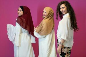 group portrait of beautiful muslim women two of them in fashionable dress with hijab isolated on pink background representing modern islam fashion and ramadan kareem concept photo
