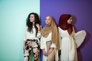 Group portrait of beautiful muslim women two of them in fashionable dress with hijab isolated on colorful background representing modern islam fashion and ramadan kareem concept photo