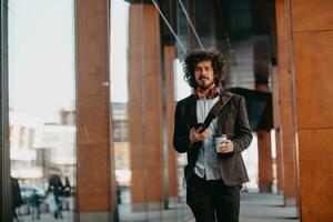 Trendy businessman with leather briefcase in financial district using smartphone while listening audio songs headphones drinking coffee photo