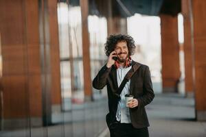 Trendy businessman with leather briefcase in financial district using smartphone while listening audio songs headphones drinking coffee photo