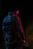 Army soldier in Combat Uniforms with an assault rifle and combat helmet night mission dark background. Blue and purple gel light effect. photo