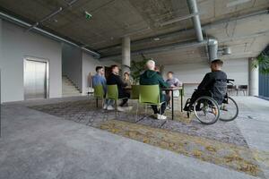 A diverse group of business professionals, including an person with a disability, gathered at a modern office for a productive and inclusive meeting. photo