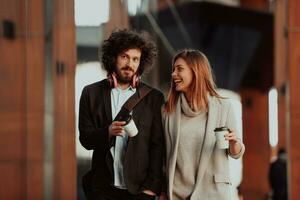 two people on a break from work walk in front of a modern company where they work and drink coffee. photo