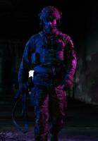 Army soldier in Combat Uniforms with an assault rifle and combat helmet night mission dark background. Blue and purple gel light effect. photo